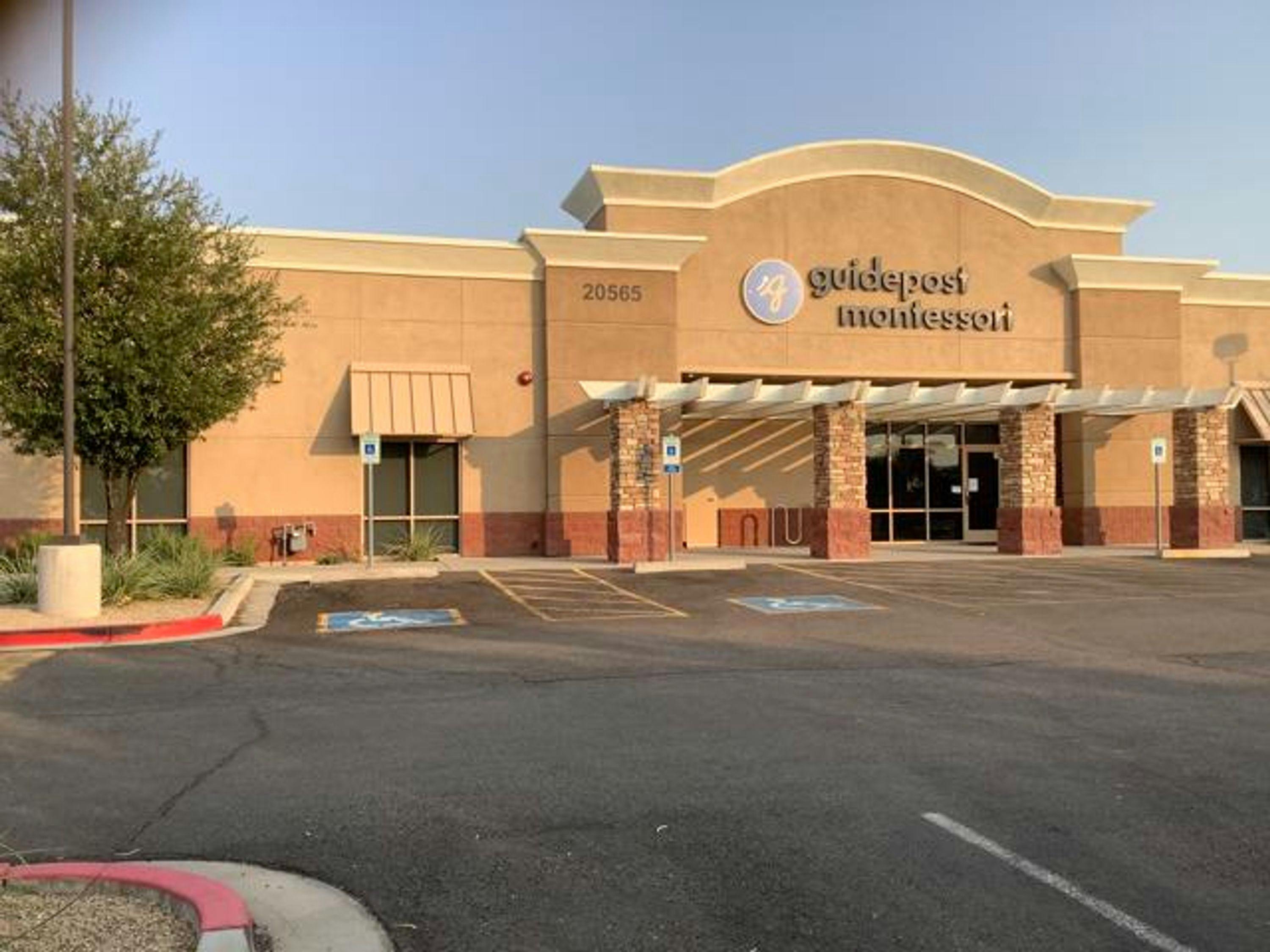 View of Guidepost Montessori at Peoria from the parking lot that shows the handicap parking spots in front of the building as well as the windowed door to the entrance below the branded Guidepost Montessori sign.