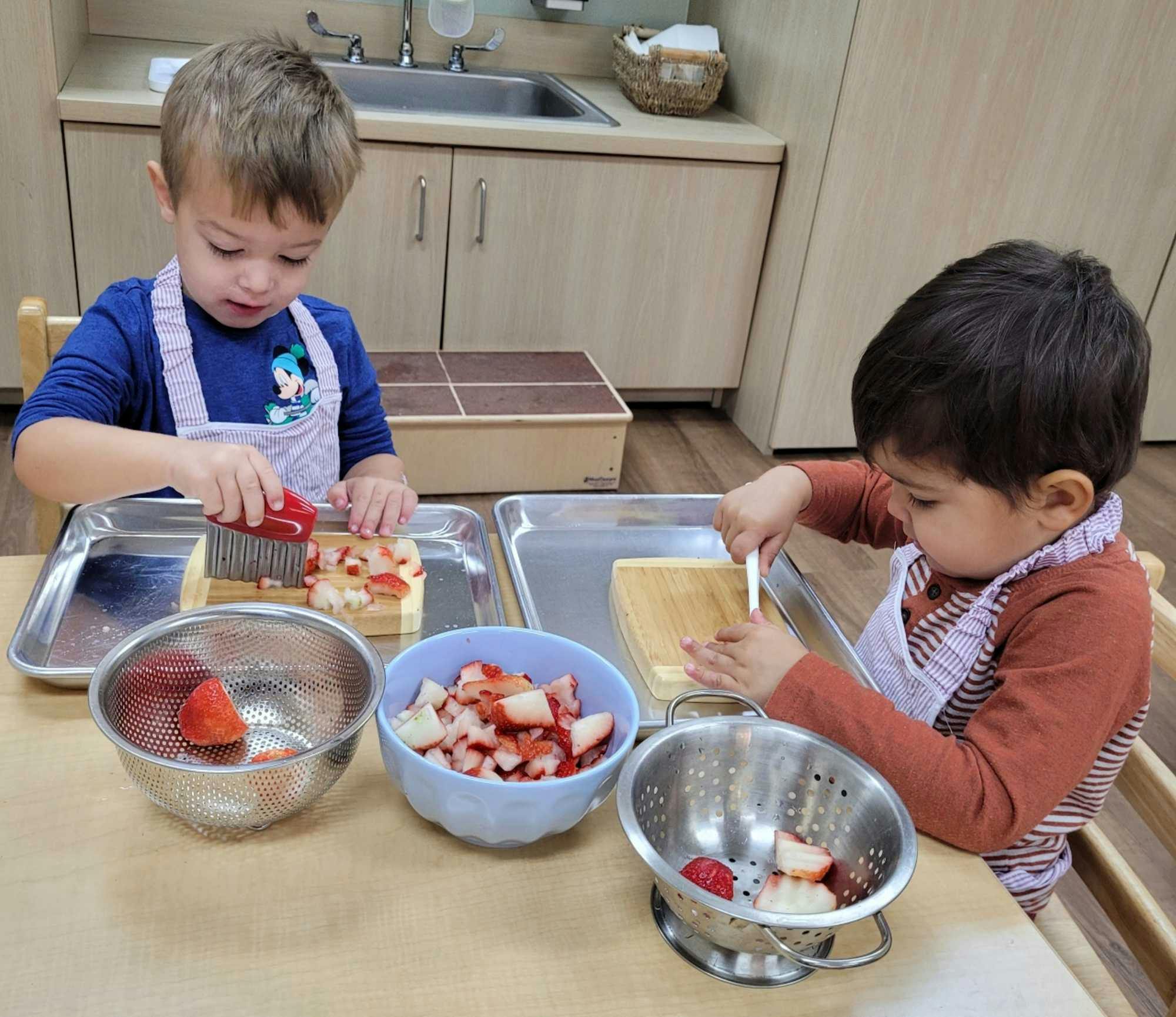 two boys sitting at a table in a Guidepost Montessori kindergarten classroom cutting fruit