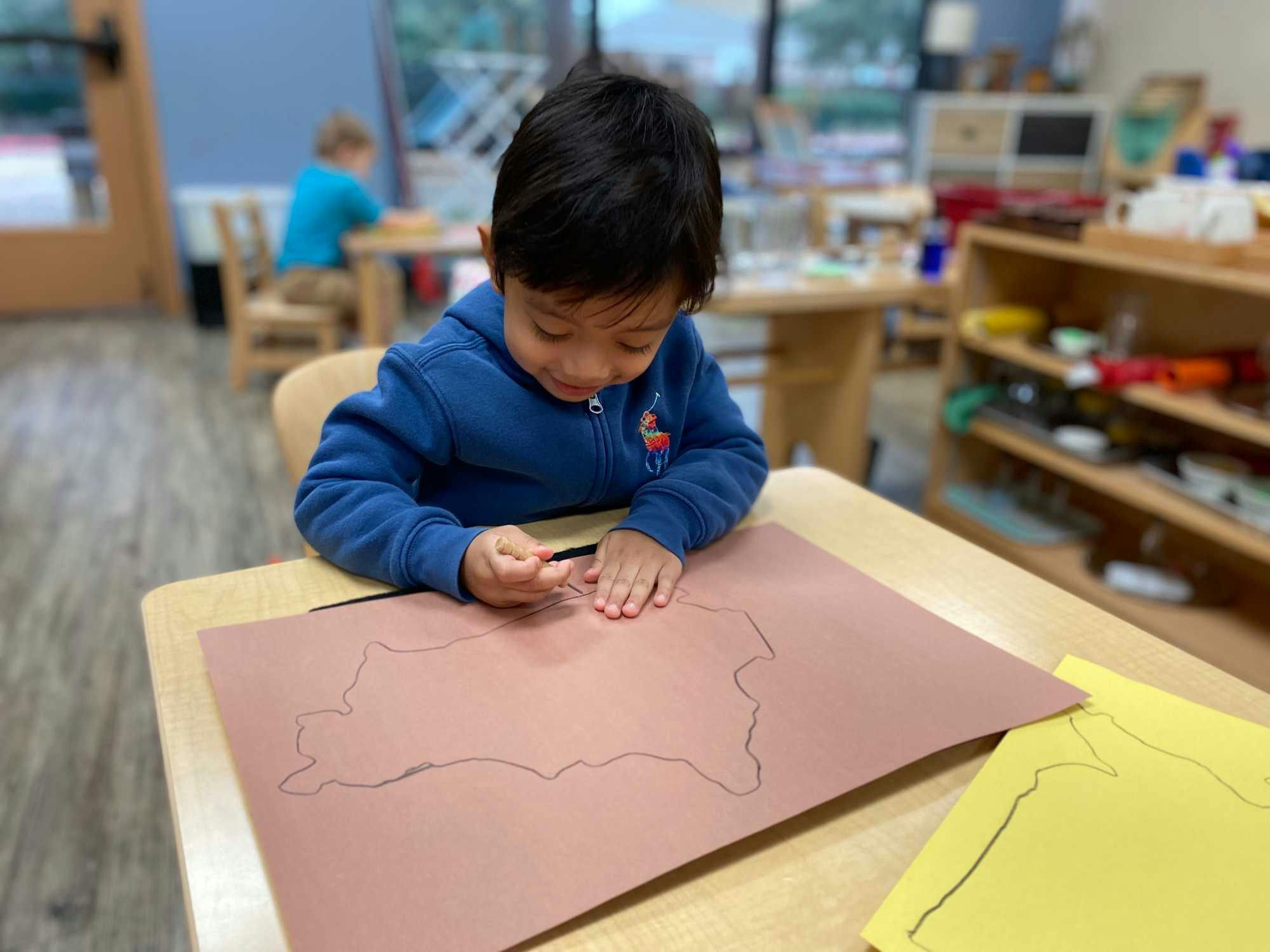 kindergarten-aged child draws map of United States of America in a well-organized Montessori classroom.