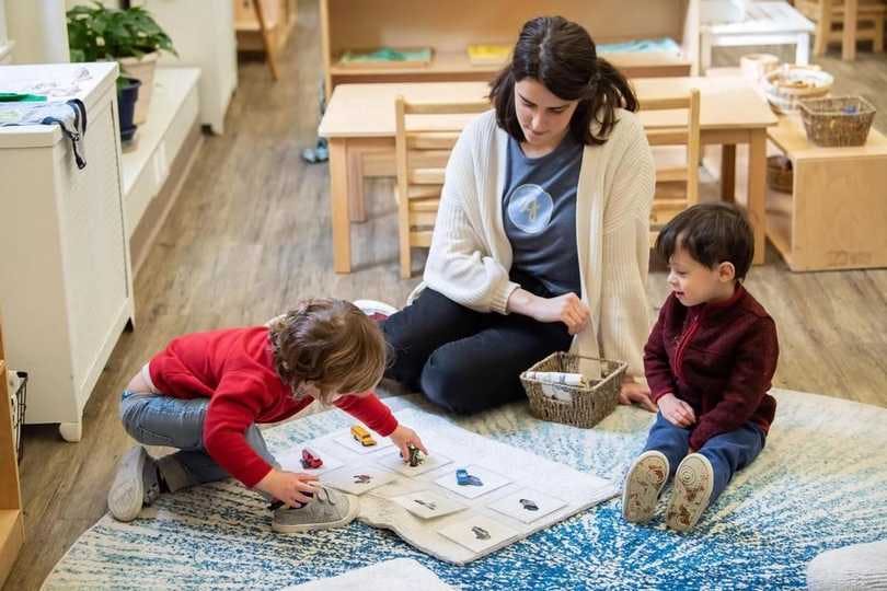  One guide watches as two preschool aged students complete a Montessori classroom activity.