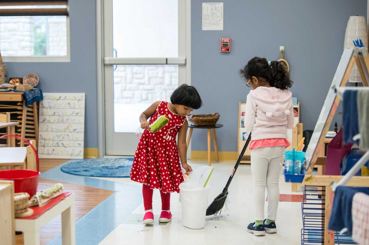 children at guidepost montessori sweeping and placing trash into can