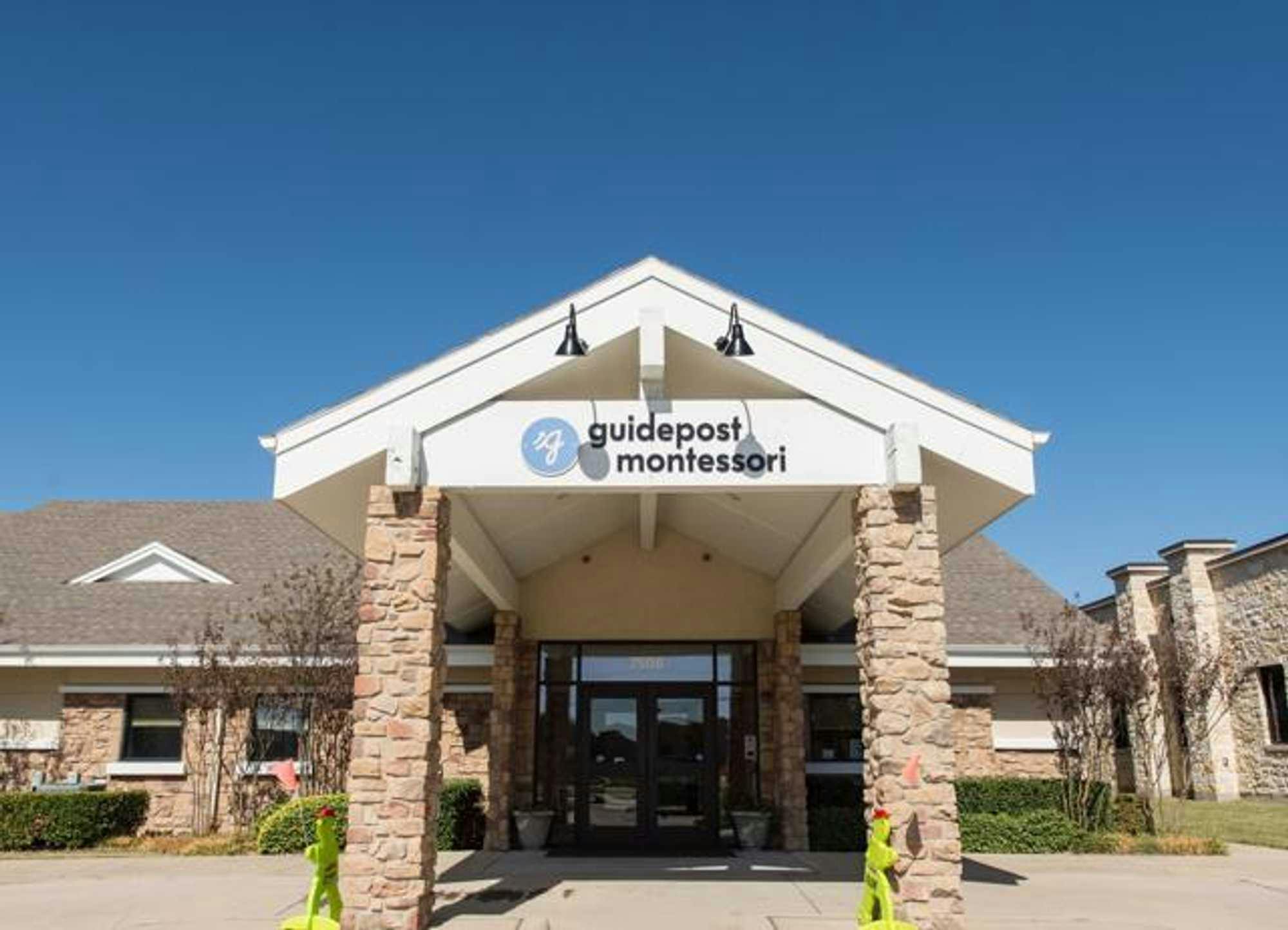 View of Guidepost Montessori at Eldorado from the pillared entryway that shows the stone exterior and entrance door, as well as a branded Guidepost Montessori sign.
