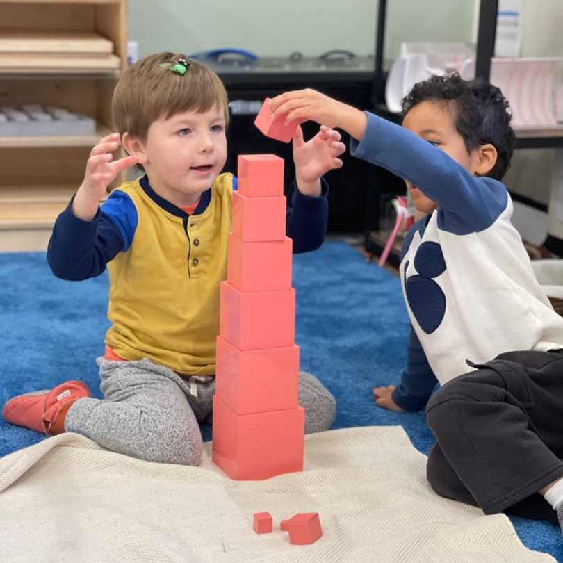 One guide watches as two preschool aged students complete a Montessori classroom activity.