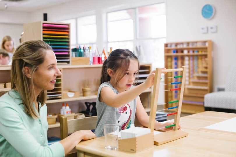 One guide watches as two preschool aged students complete a Montessori classroom activity. 